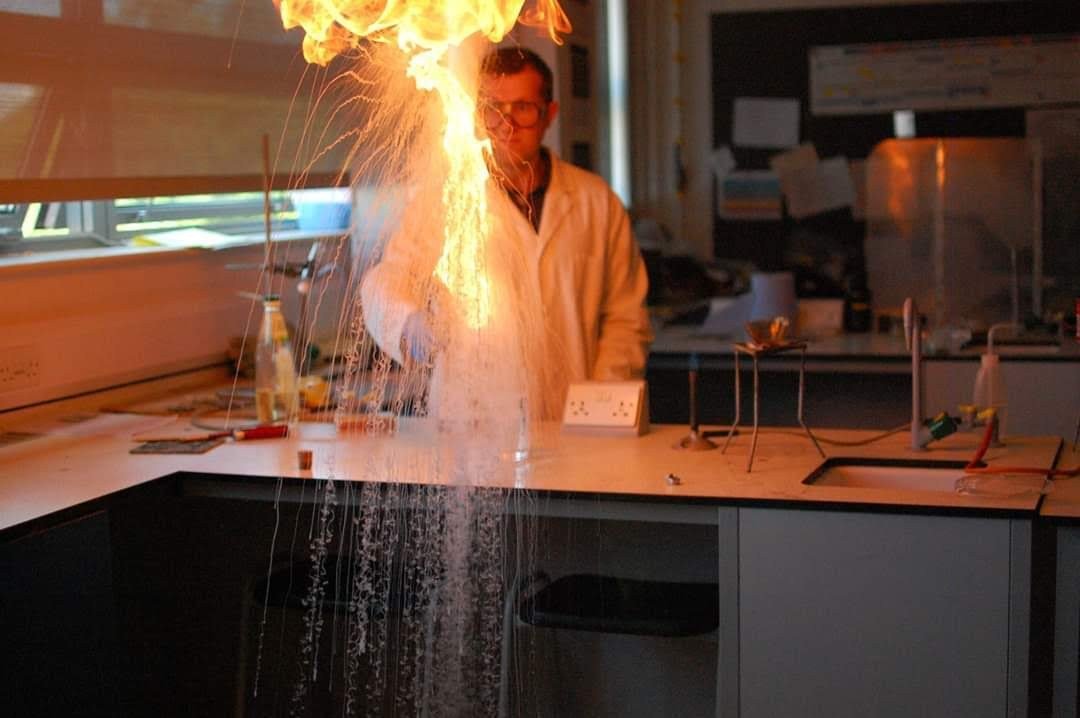 A chemistry demonstration in a school laboratory, with a bright flame and sparks above the bench